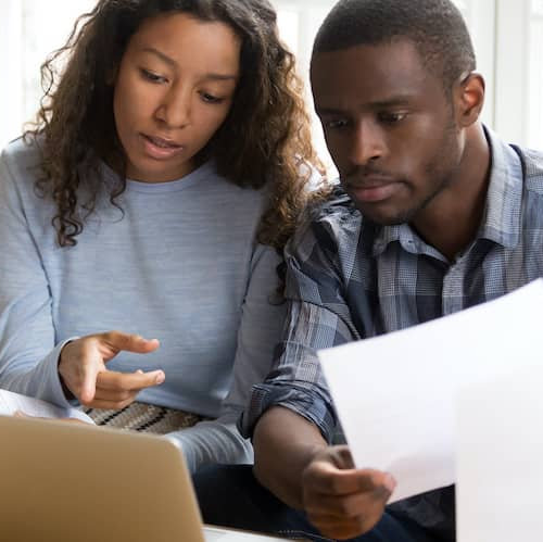 Couple reviewing documents on laptop, possibly home related.