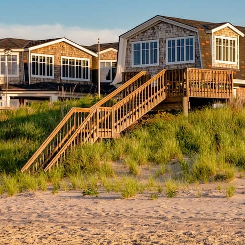 A couple of beachfront homes with wooden stairs leading to the sand.