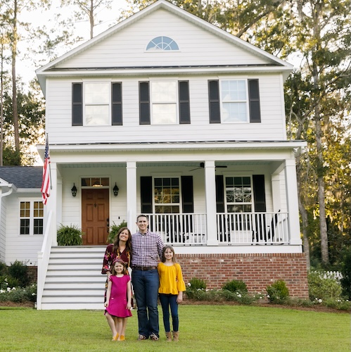 Family with two young children in front of a large farmhouse.