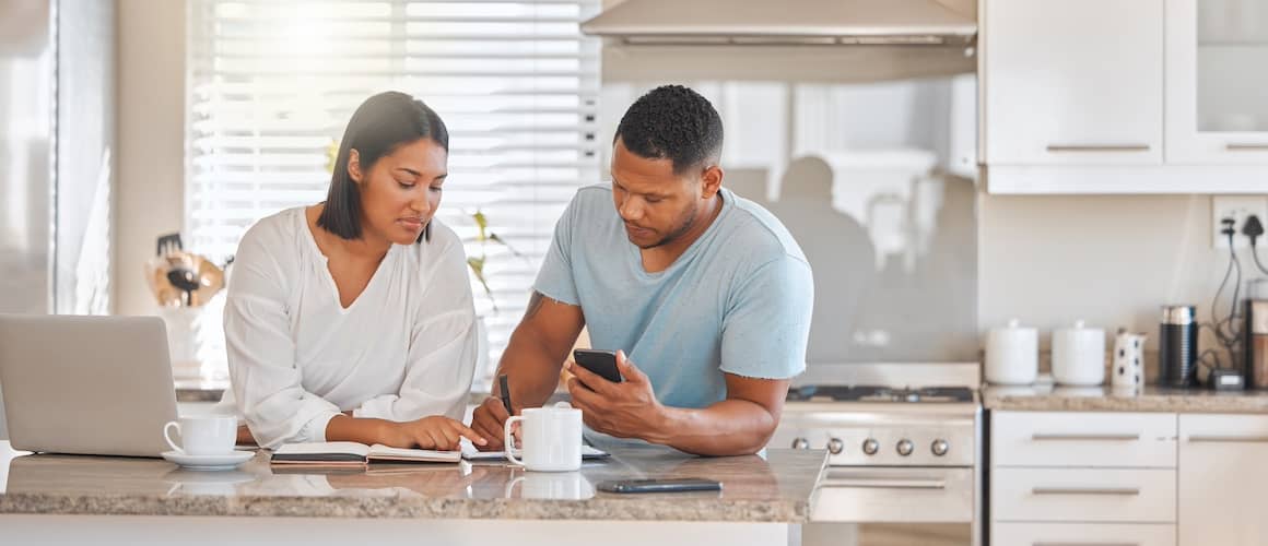 Young couple standing in their kitchen together looking over papers on the counter.