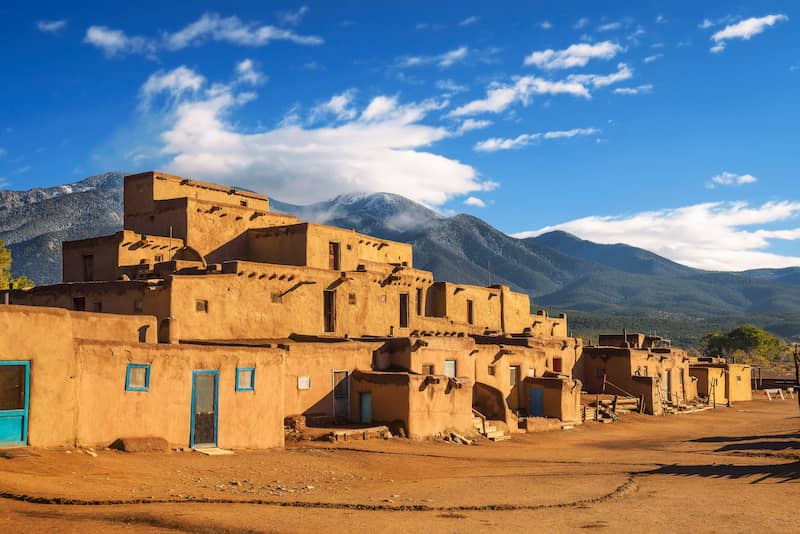 Rectangular buildings in Tao, New Mexico with mountains in the background.