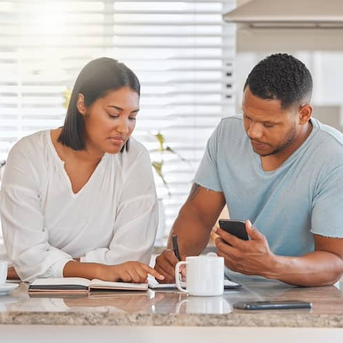 Young couple standing in their kitchen together looking over papers on the counter.