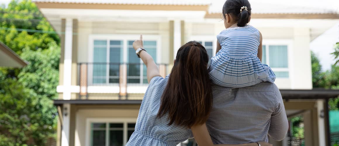 A couple with a child looking at the exterior of a house.