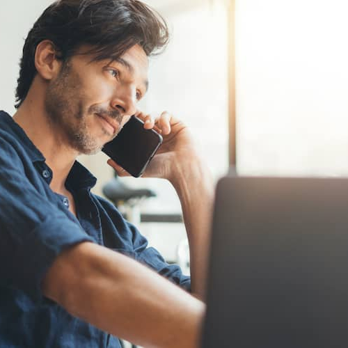 A person talking on phone while also working on his laptop.