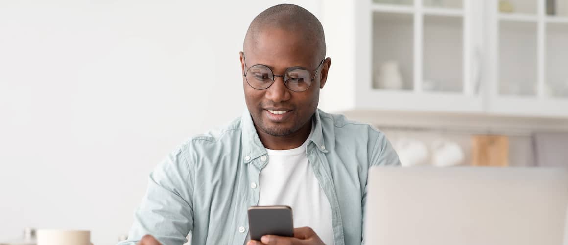 Man checking his phone while using calculator and laptop.