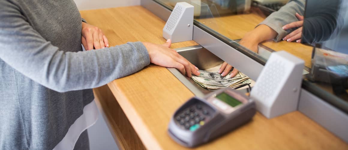 A bank clerk behind glass handing money to a customer on the other side.