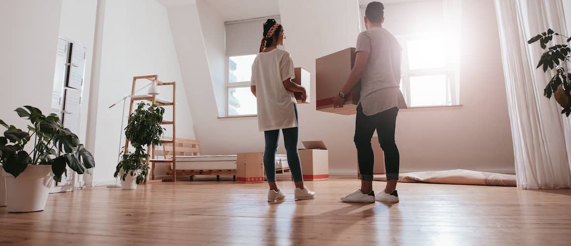 Couple moving into new home, unloading boxes into   open airy living room with multiple potted plants.