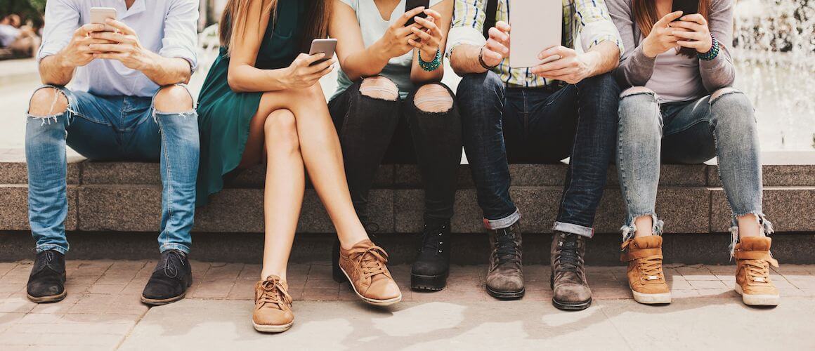 Young people sitting in a line and using phones.