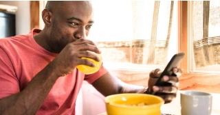 Un hombre bebe jugo de naranja mientras mira su teléfono móvil.