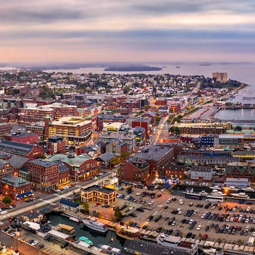 Portland Maine at dusk lit up by building and streetlights and with water in the background.