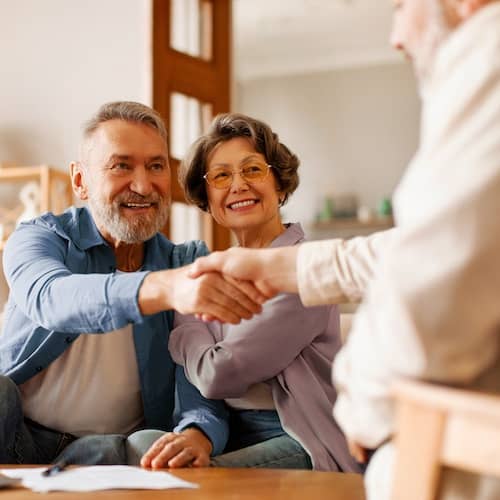 Couple shaking hands with an agent, presumably after signing the paperwork laid out in front of them.