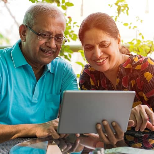 Close-up of older couple in glasses reviewing financial documents at dining table.