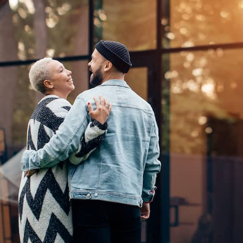 A couple standing outside their house, with a car parked in the driveway.
