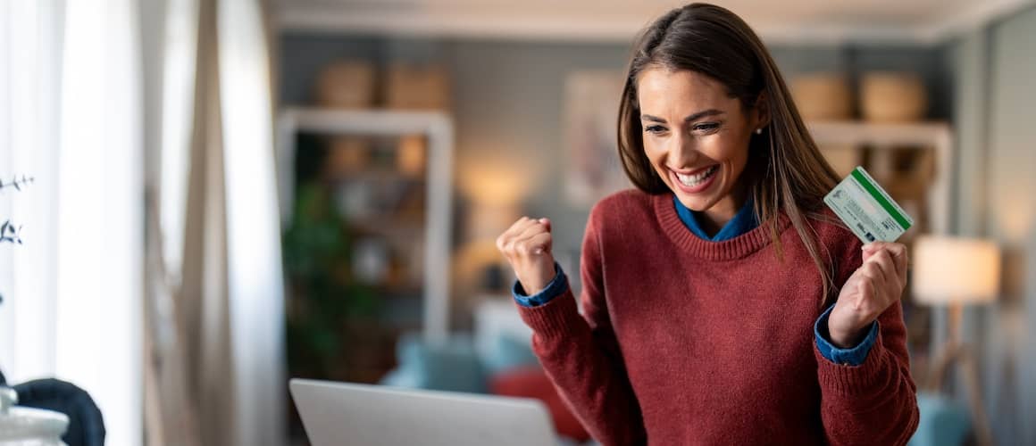 woman feeling excited looking at laptop screen holding credit card