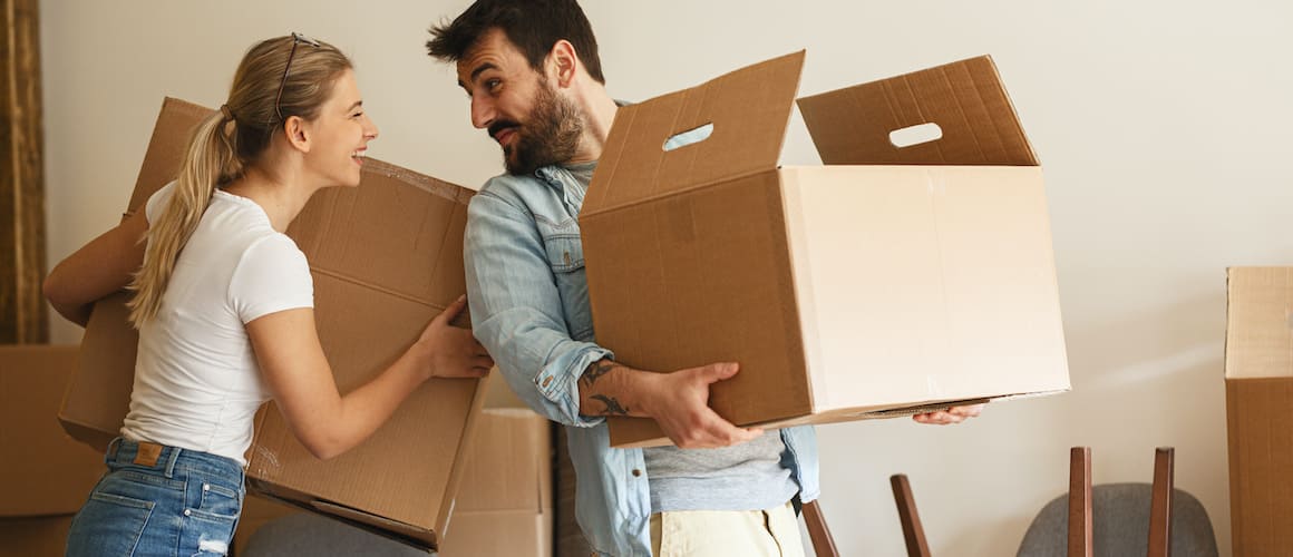 Image depicting a couple during the process of moving into a new home, with boxes and furniture being transported.