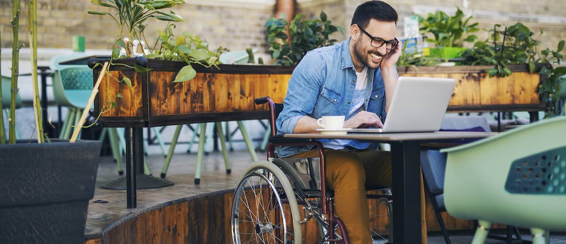 Man in a wheelchair on computer at cafe.