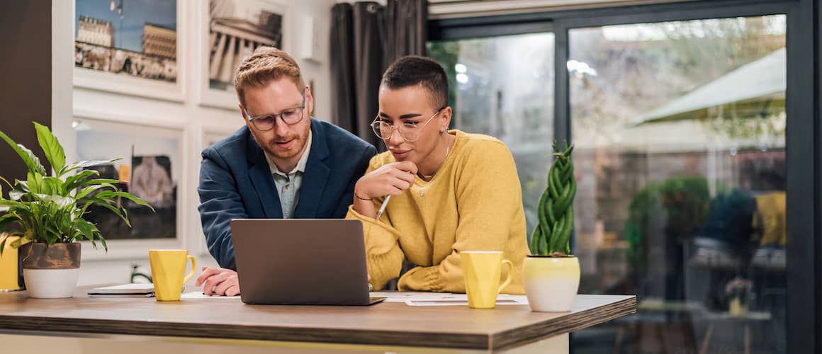 Young couple sitting at a kitchen counter with a laptop, potentially discussing finances or real estate options.