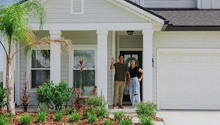 Couple smiling and waving from the door of their green pastel colored home.
