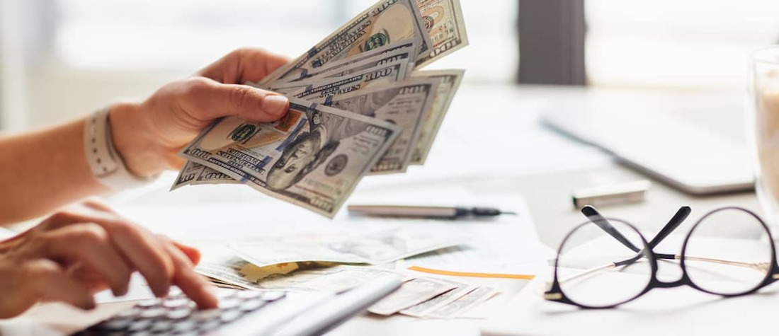 Woman holding cash and using calculator.