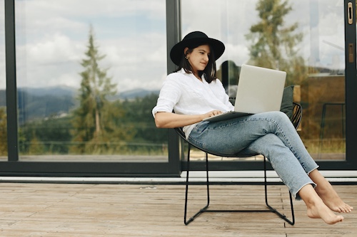 Young woman sitting on back deck on laptop.