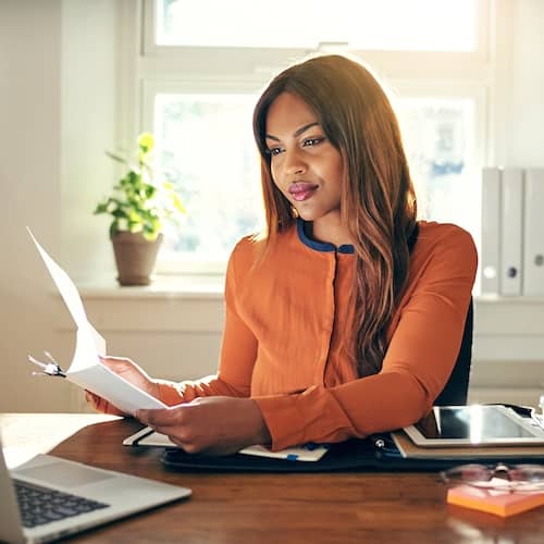 Young woman reviewing paperwork in front of a laptop.