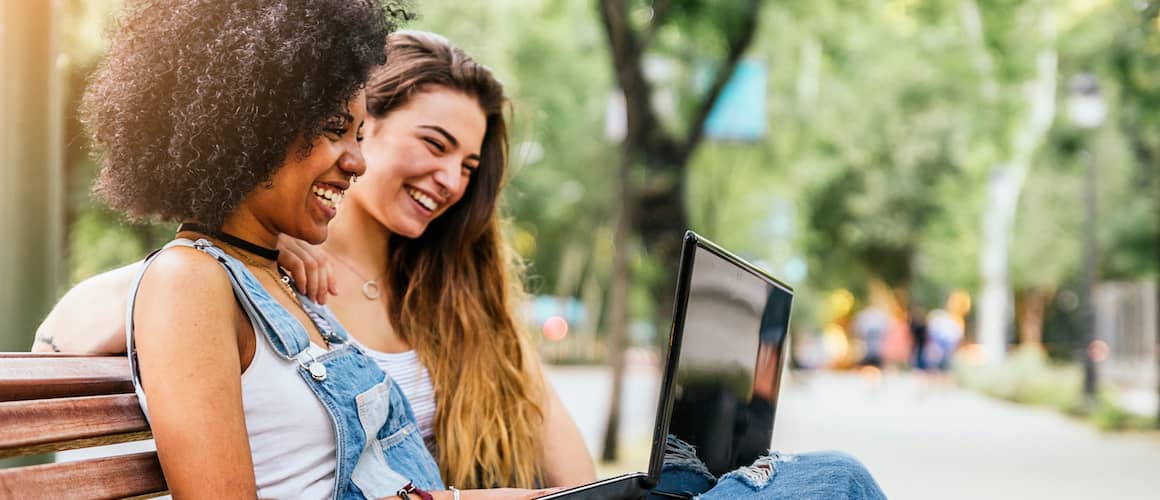 Two women using a laptop together on a bench, potentially working on financial or real estate matters.