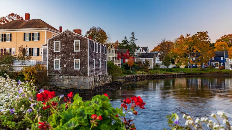 A couple of buildings near a body of water with flowered bushes in New Hampshire.
