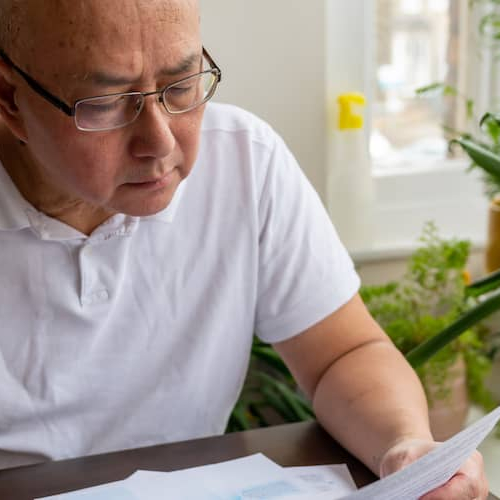 A senior man seated at a table, possibly reviewing bills or managing finances.