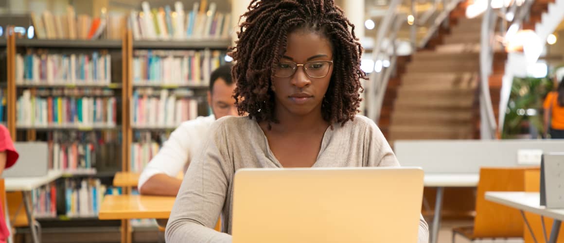 Young African American student using her laptop in a library.