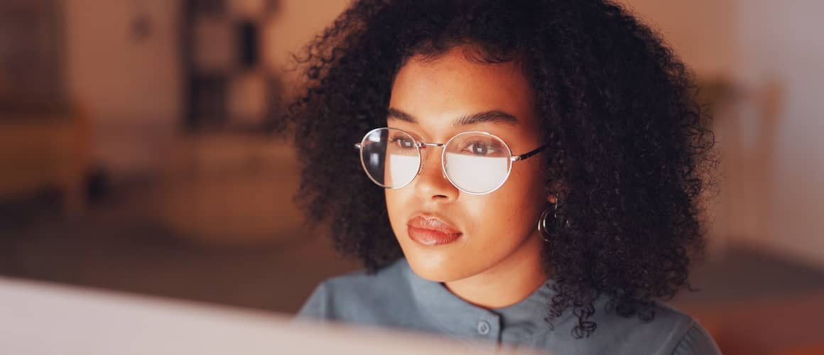 Young woman wearing reading glasses viewing information online at desktop computer.