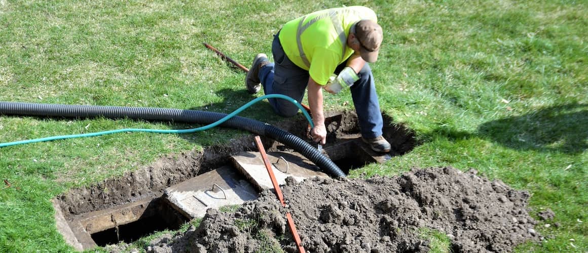 Worker wearing a safety vest pumping a homeowner's septic tank in their backyard.