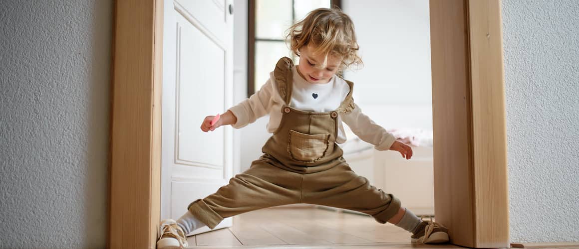 A kid doing a split in the doorway of a house.