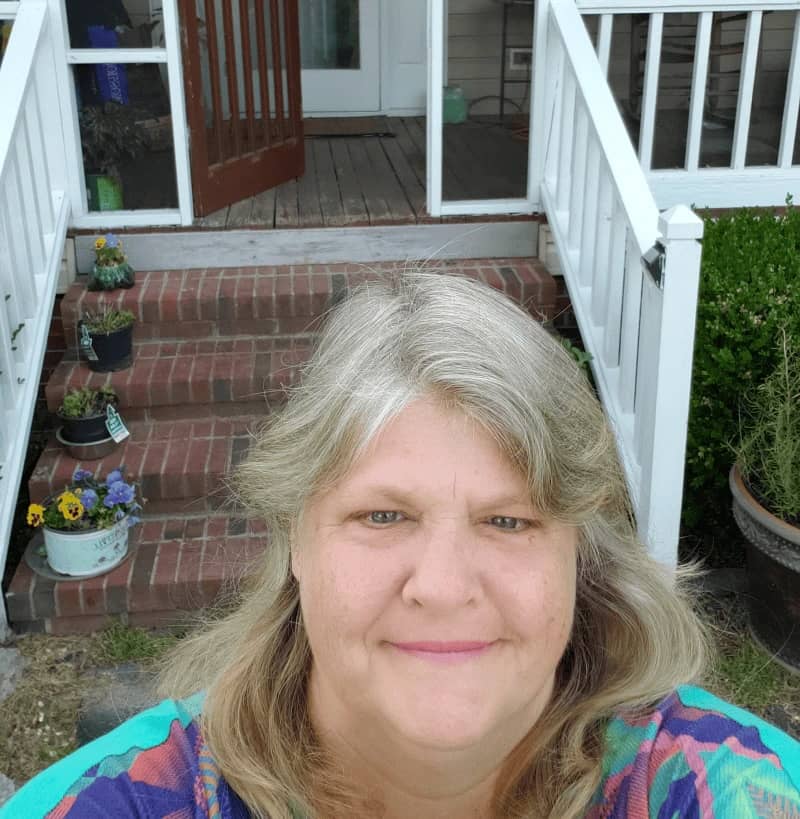 Woman taking a selfie in front of a set of brick steps leading to a screened in patio.