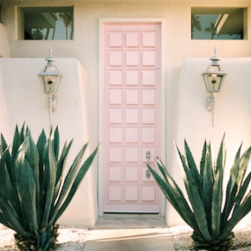 Pink MCM doorway to stucco home exterior with southwestern landscaping flanking doorway.