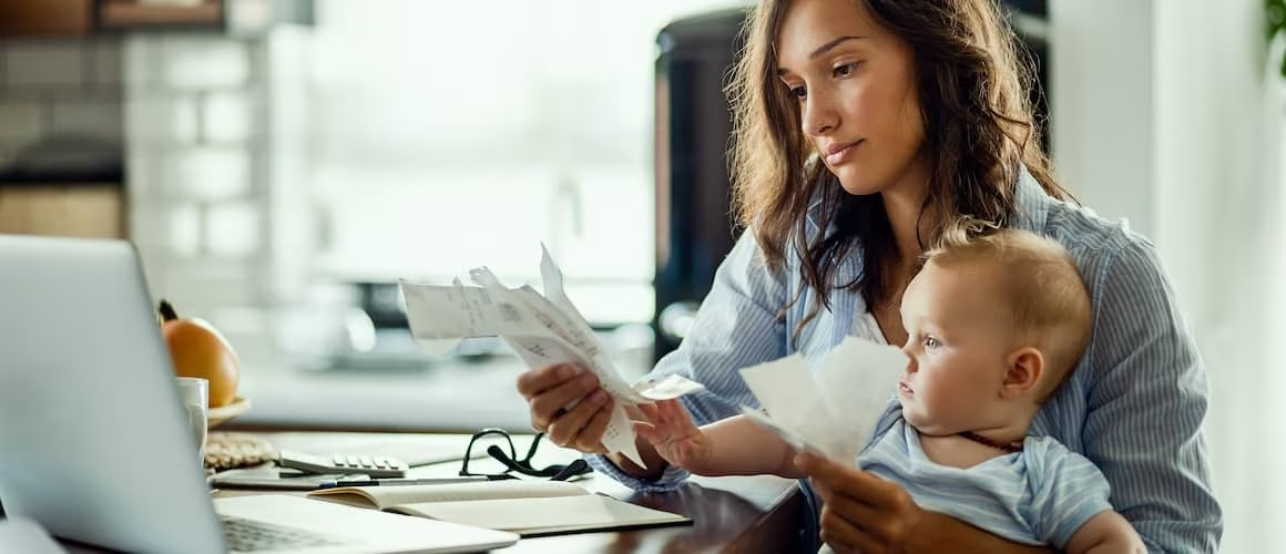 Young mother sitting at a table wit her baby, looking at mail.