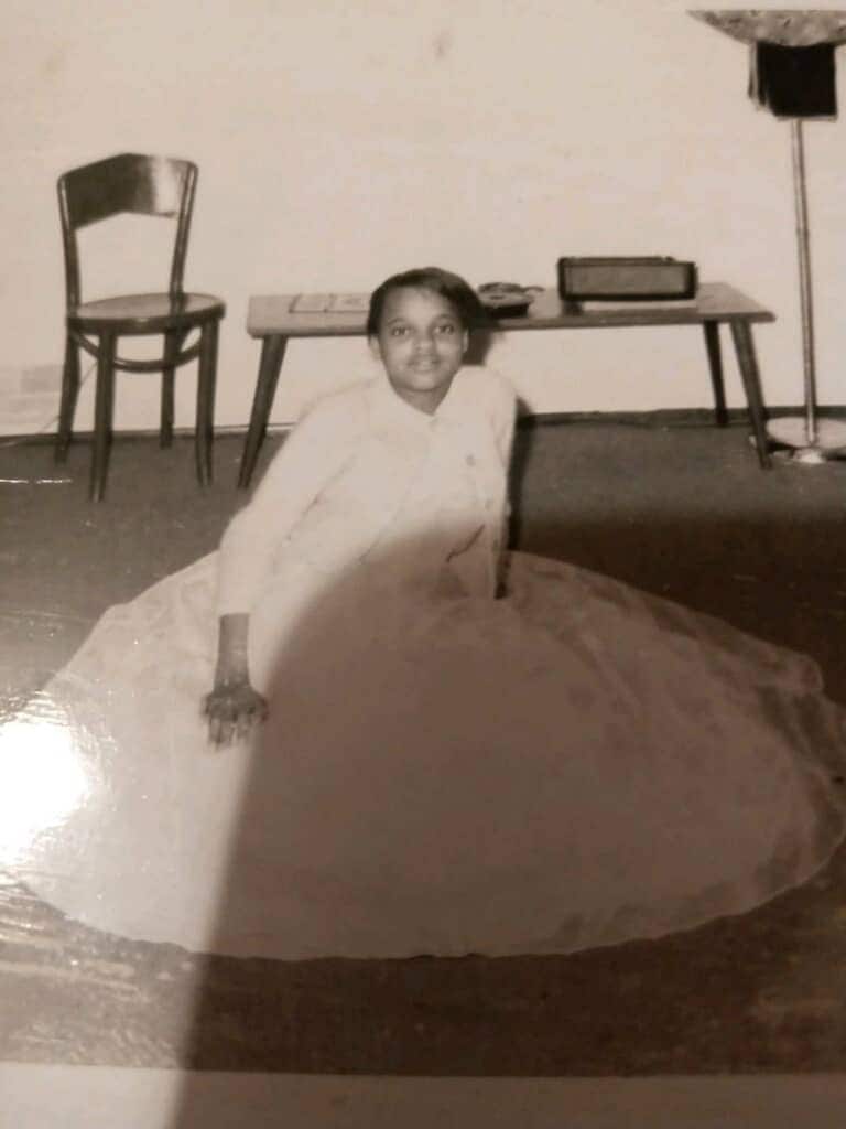 Black and white photo of a young woman sitting on the ground in a dress.