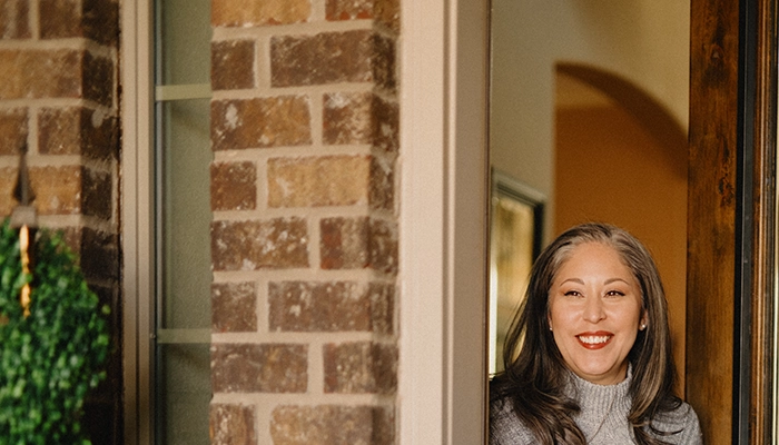 Woman opening door to brick house smiling.
