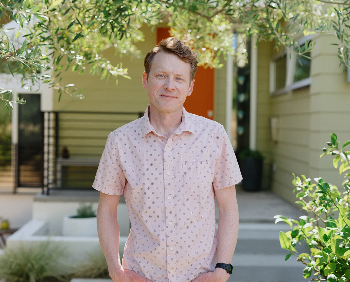 Man standing outside a home in a pink shirt.