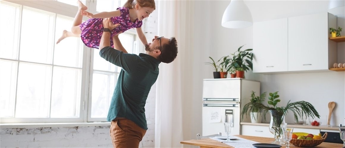 Image of smiling father lifting daughter in kitchen.