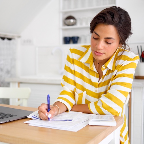 Woman in yellow striped shirt calculating her budget at the kitchen table.