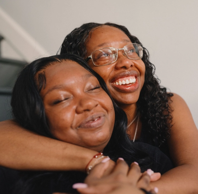 A Black mother and daughter hug by the staircase of their new home.