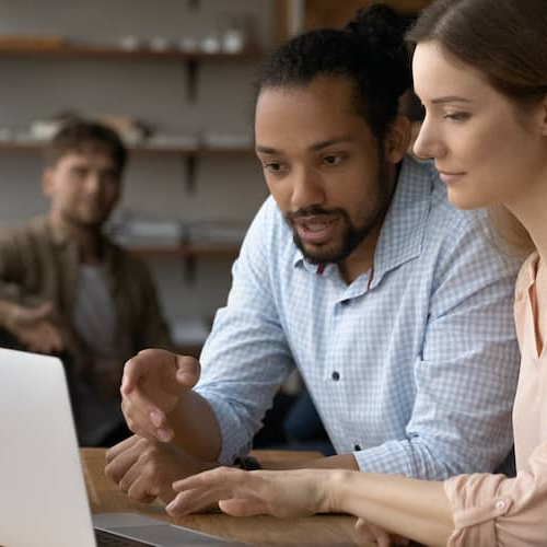 Male loan officer carefully explaining mortgage details on computer screen to engaged woman customer.