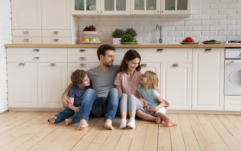 Family sitting on the hardwood floor in bright kitchen.