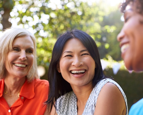 Older female friends hanging out on back patio and smiling.