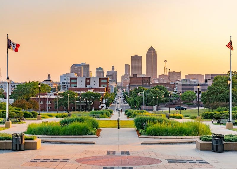 Wide view of a downtown in Polk County Iowa featuring a grassy town square leading to a long boulevard toward the skyline.