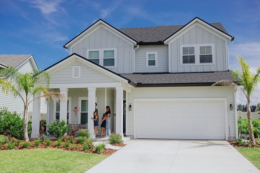 Light gray two-story house with a front porch and garage, with a family standing on the front porch.