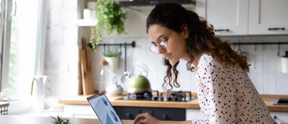 Woman sitting at kitchen table working on laptop.