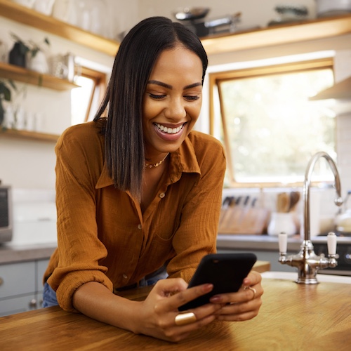 Woman leaning on kitchen island looking at her phone and smiling.