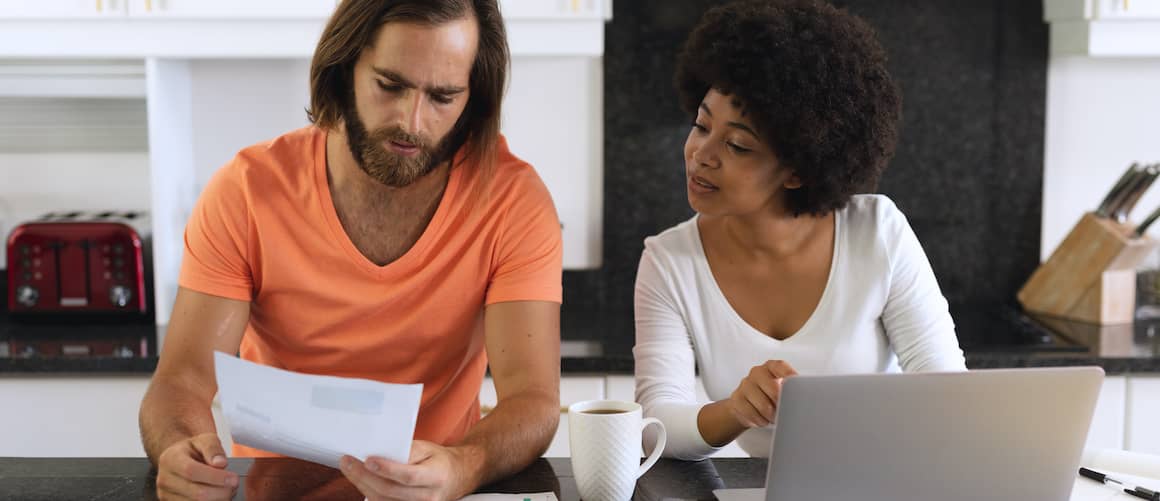 Diverse Couple Sitting In Kitchen Using Laptop