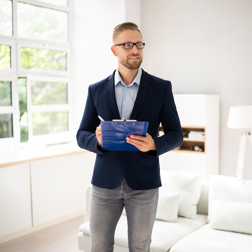Man in suit jacket with clipboard appraising a home while standing in the living room.